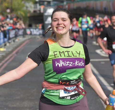 A runner in a green Whizz Kidz top runs with her arm out smiling
