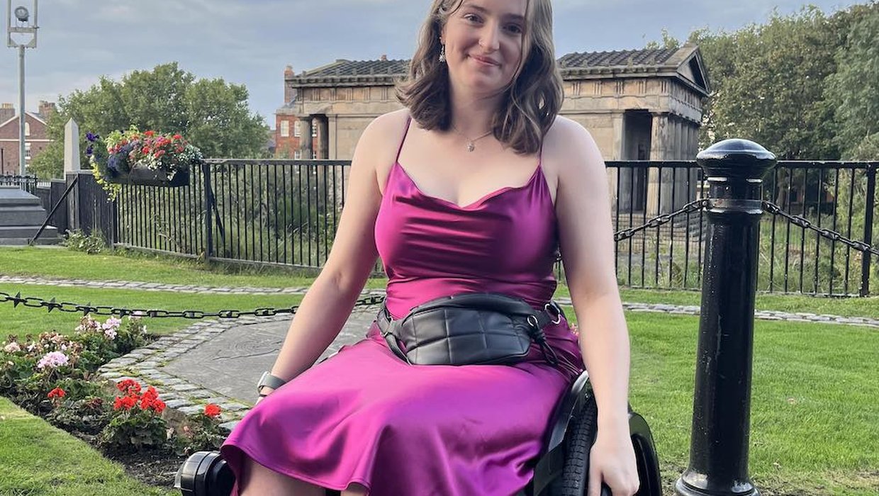 Ella from Kidz Board outside in a garden. She is wearing a purple evening dress. She's in her black wheelchair.