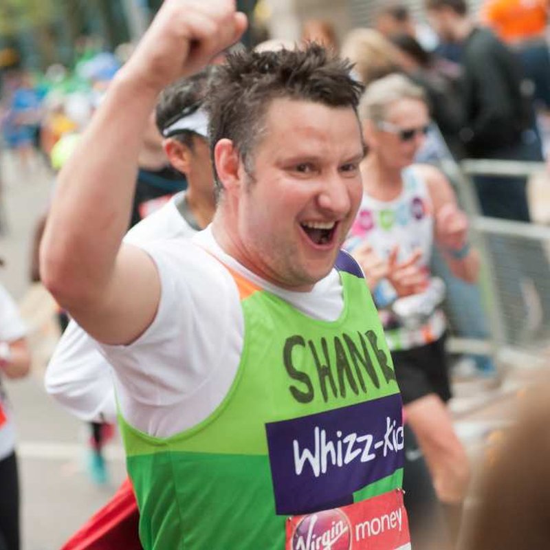 A runner in a green Whizz Kidz top raised his arm as he runs past the camera