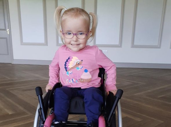 A young wheelchair user in an awesome pink wheelchair smiling