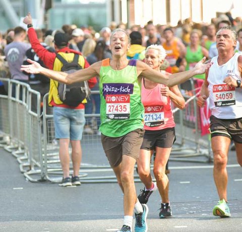 A runner in a green Whizz Kidz top holds his arms out as he soaks up the atmosphere