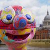 Jason Wilsher-Mill's Morph's head in close up. He is in front of the river Thames, with London skyline behind him. Morph's head features an intricate psychedelic pattern, including stars on his eyes and a union flag mask.